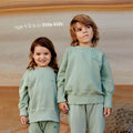 Young boy and girl wearing a sustainable green kids' jumper by Earthlings United, made from soft organic cotton for comfort and durability